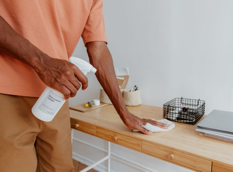 A professional cleaner wiping down desks in a bright, modern office