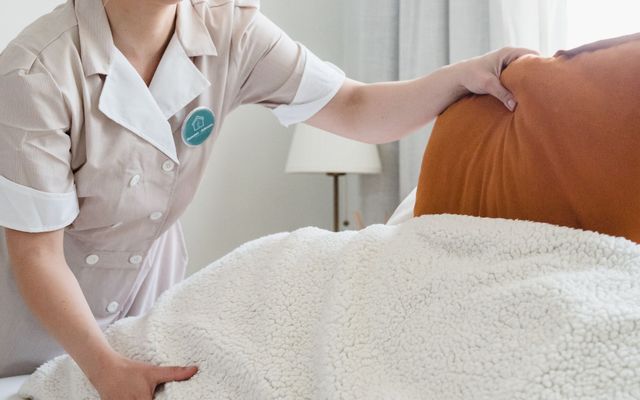 A housekeeper making up a bed with fresh linen in a bright room