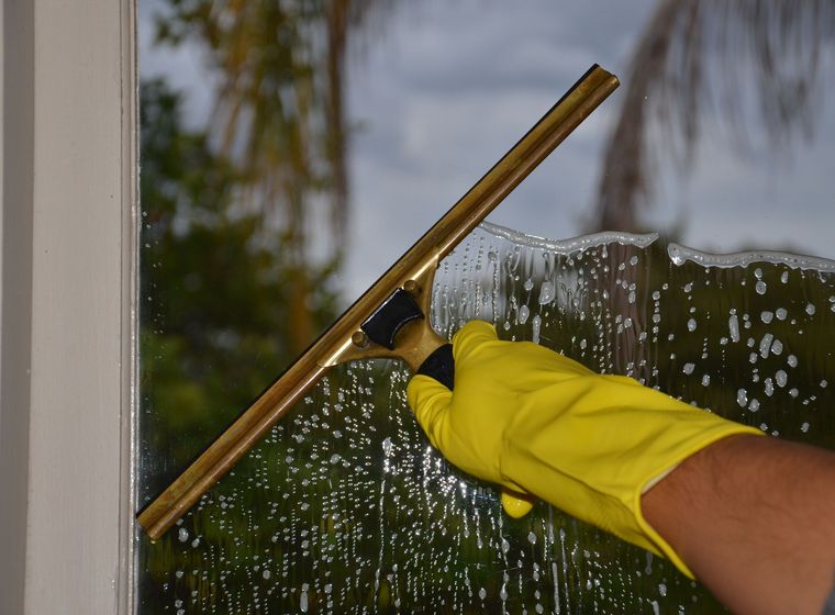 A professional cleaner pulling a squeegee across a large window, leaving it streak-free